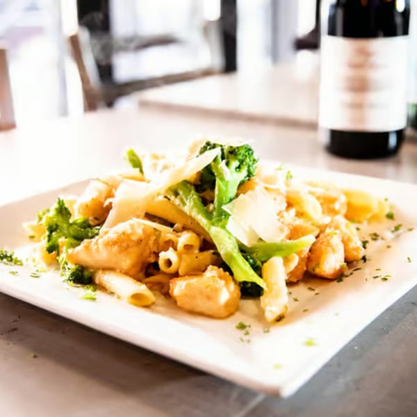 Rocco's penne pasta with chicken, broccoli, and parmesan cheese, with a wine bottle in the background.
