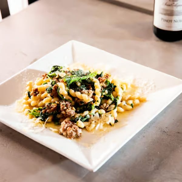 Rocco's Italian pasta dish with sausage, spinach, and grated cheese on a white plate.