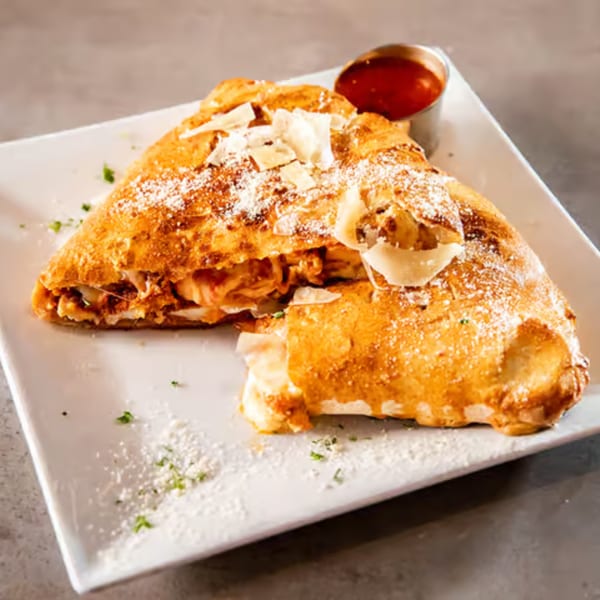 A golden-brown calzone, cut open to reveal its cheesy filling, served with a side of marinara sauce.