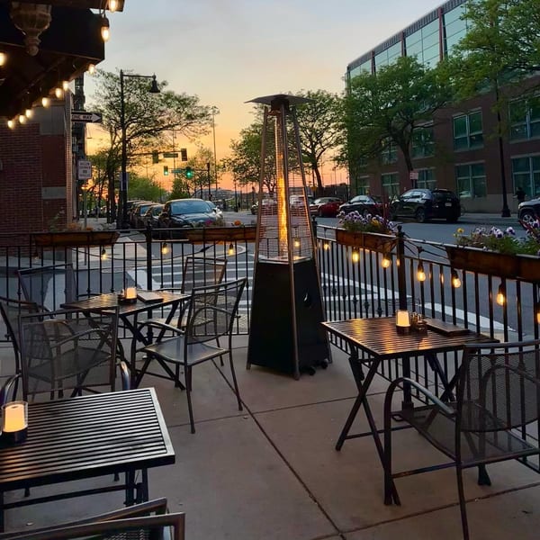 Rocco's outdoor patio at dusk with metal tables, chairs, a patio heater, and string lights.
