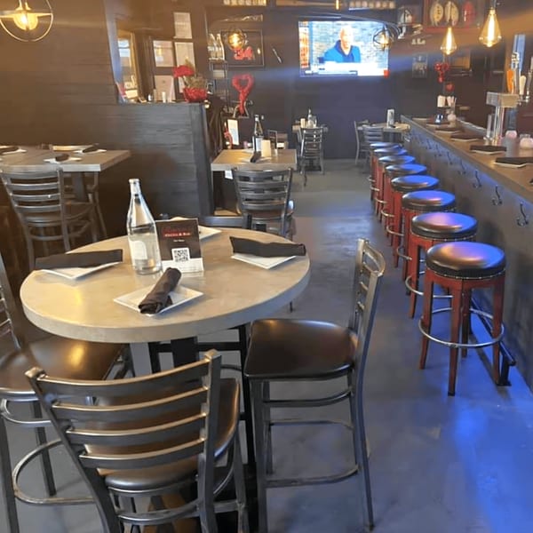Interior of Rocco's Cucina & Bar, showing dining tables, bar stools, and a television screen.